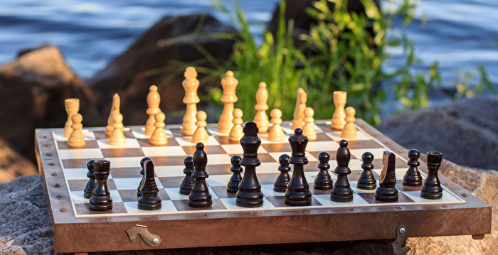 Chess board with chess pieces on rock with river embankment background. Selective focus on black pieces. Outdoors chess game
