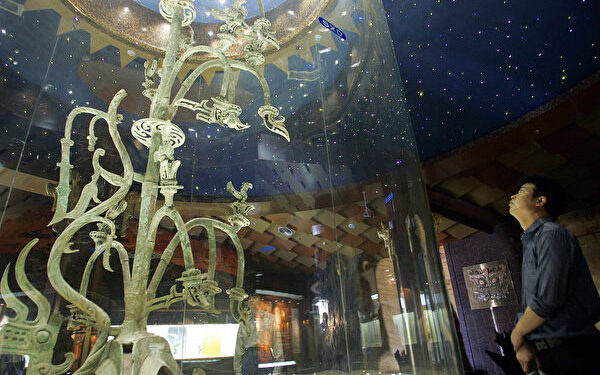 GUANGHAN, CHINA: A visitor looks at a relic of bronze tree at the Sanxingdui Museum in Guanghan city, in China's southwestern province of Sichuan, 28 May 2005. Day after sweltering day on the banks of the Modi stream, archeologists are dealing shattering blows to traditional views of Chinese history as they work their way through the parched, yellow earth. AFP PHOTO/LIU Jin (Photo credit should read LIU JIN/AFP via Getty Images)