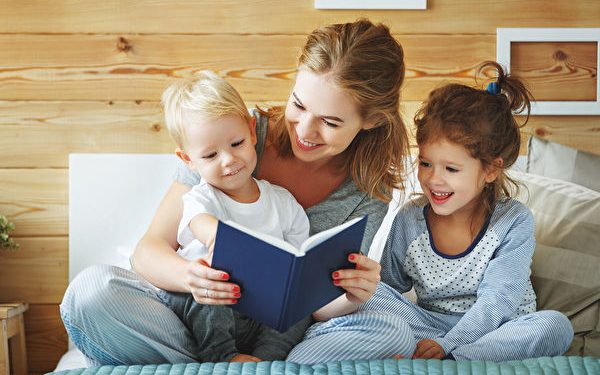 happy family mother reading to children book in bed